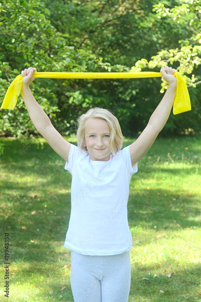 Beautiful school aged kid girl plays sports with a latex band outdoors in the park. Healthy lifestyle. Beautiful school aged kid girl plays sports with a latex band outdoors in the park. Healthy lifestyle.