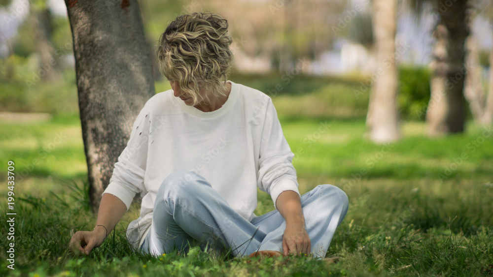 Obraz premium A blonde young woman sitting on the grass in the park in the spring time.