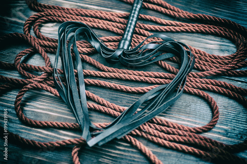 Scourge for BDSM in the form of a heart and a rope for binding on a dark background. Accesories for sexual games.