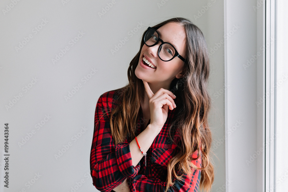 Portrait of young brunette stylish girl with nude make up and wonderful  smile smiling and feels happy, keeps teeth clenched. Isolated over white  wall near the window Stock Photo | Adobe Stock