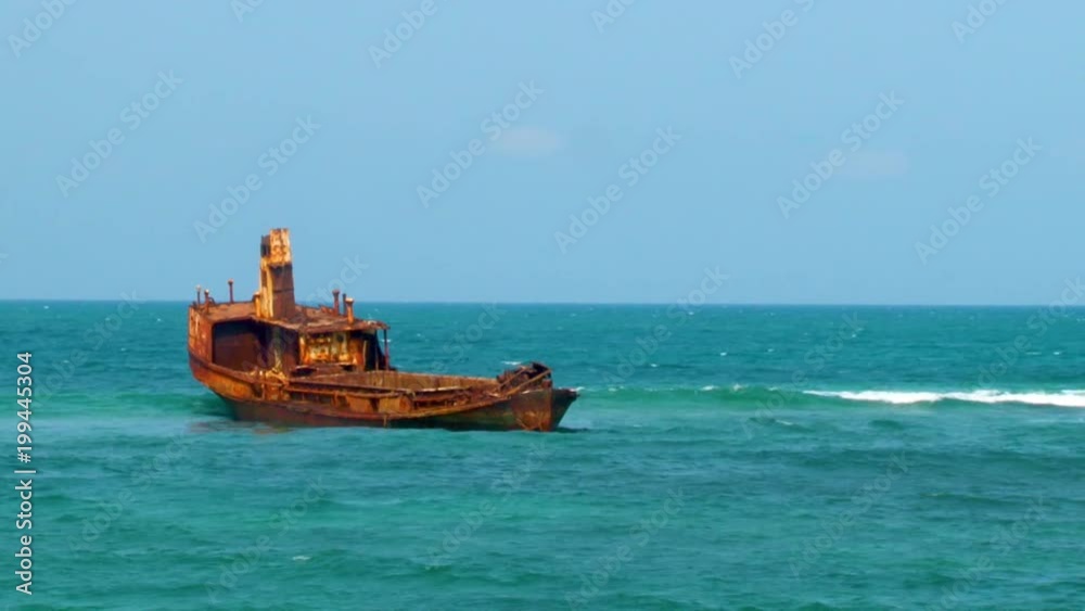 An abandoned, rusted boat sits in shallow waters off the coast of Africa An abandoned, rusted boat sits in shallow waters off the coast of Africa