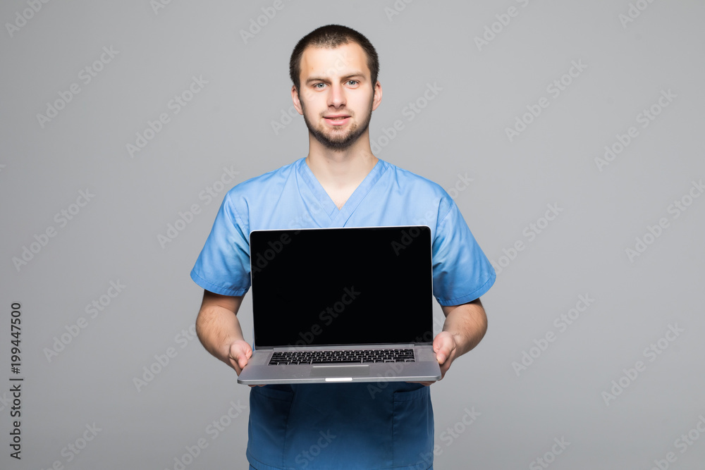 Portrait of a happy male doctor dressed in uniform with stethoscope showing blank screen laptop computer isolated over gray background