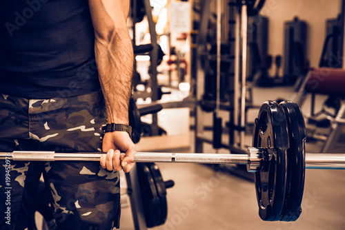 Sporty man holds barbell in gym close photo