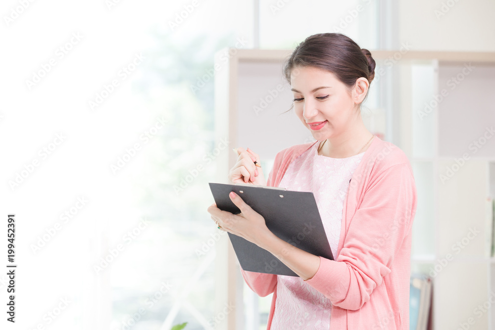 Business woman standing working near a window and holding clipboard at office. Business woman standing working near a window and holding clipboard at office.