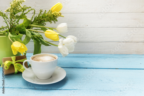 coffee cup, yellow and white tulip flowers in a green vase and a little gift on turquoise wood, white wooden background with copy space, selected soft focus, narrow depth of field