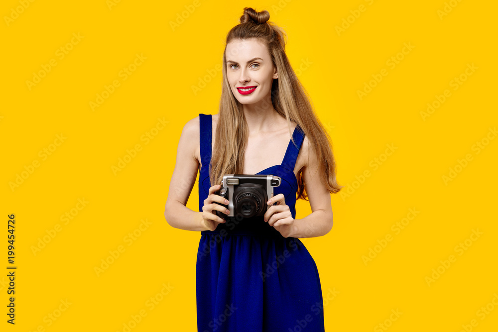 Young woman on a yellow background and blue dress is holding a camouflage and smiling. Colour obsession concept. Minimalistic style. Stylish Trendy Young woman on a yellow background and blue dress is holding a camouflage and smiling. Colour obsession concept. Minimalistic style. Stylish Trendy