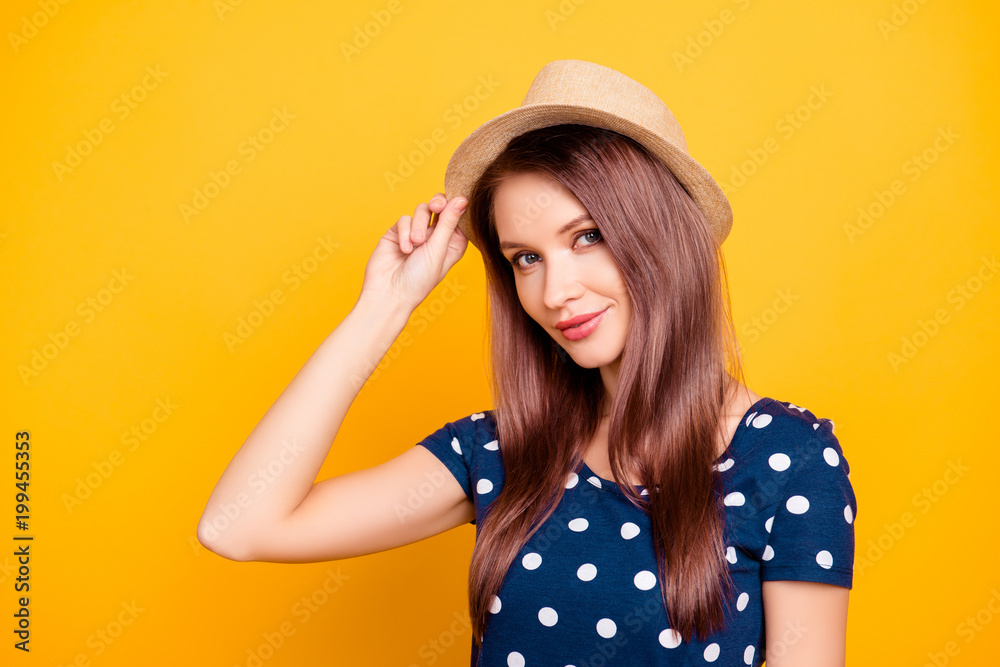 Portrait of sexy, adorable, nice, kind, pretty, lovely, professional woman, tour operator in polka-dot t-shirt holding hand on hat, looking at camera, isolated on yellow background