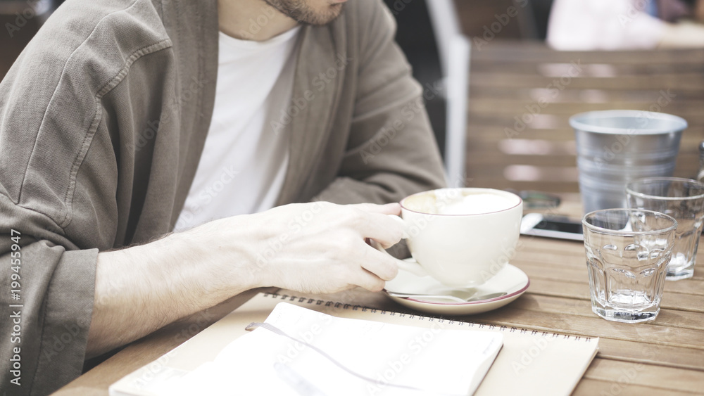 A white man is holding a cup of coffee in a white beige cup of cafe outdoors A white man is holding a cup of coffee in a white beige cup of cafe outdoors