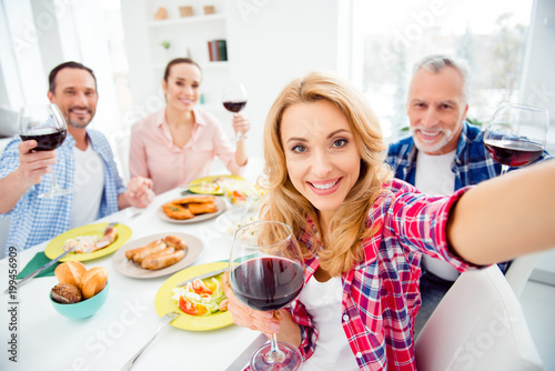 Beautiful  attractive  cheerful  stylish women shooting self portrait with her relatives  guests  visitors  meeting in house  apartment  room  sitting at the table  eating food  drinking wine