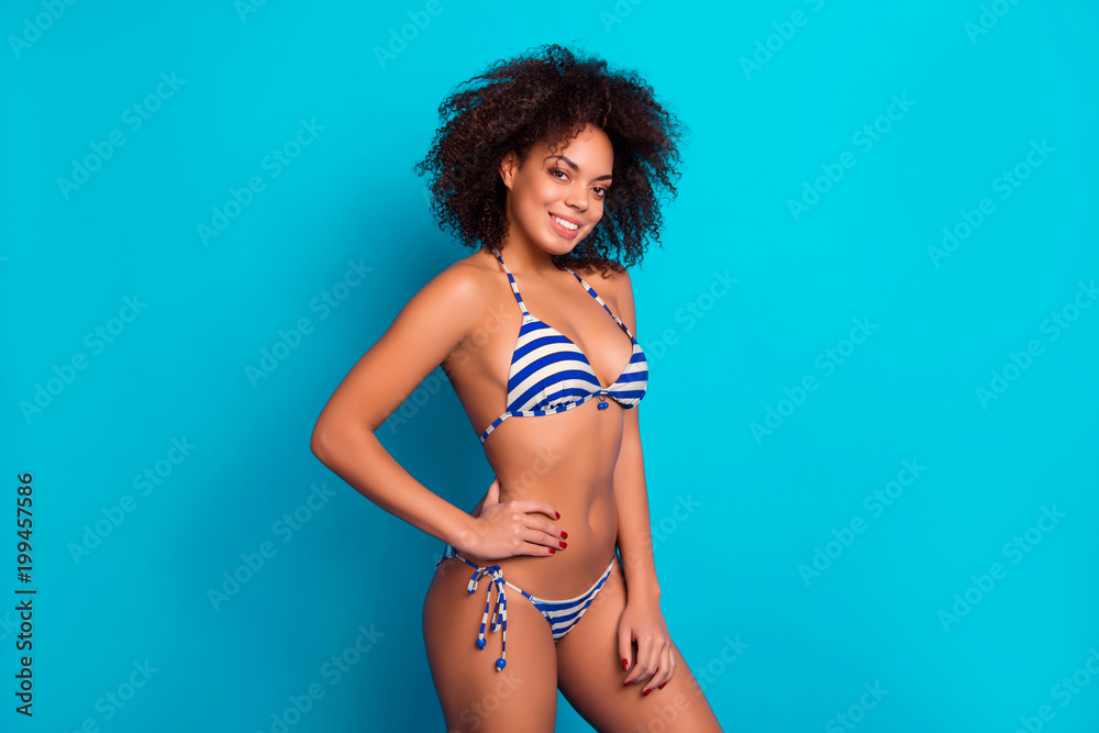 Concept of having perfect fatless slim figure in summer. Portrait of attractive confident cute lovely charming cheerful afro woman wearing striped swimsuit, isolated on blue background - obrazy, fototapety, plakaty 