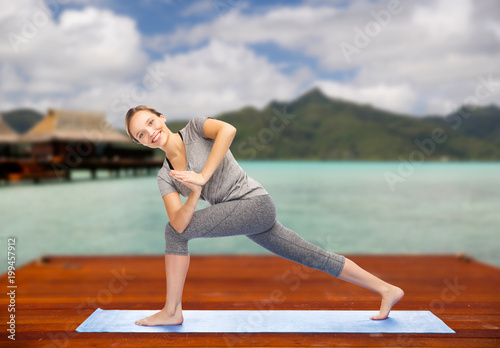 fitness, sport, people and healthy lifestyle concept - woman making yoga low angle lunge pose on wooden pier over island beach and bungalow background