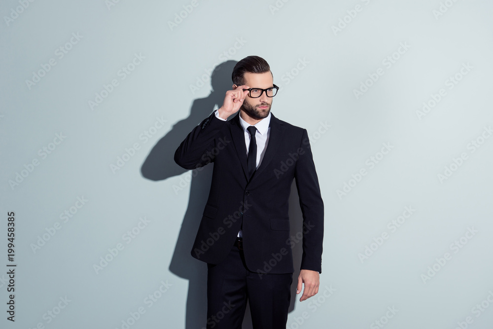Portrait of perfect, manly, thoughtful, virile, clever, confident, man in formal wear, black pants and jacket, holding eyelet of glasses on his face, looking to the side over grey background Portrait of perfect, manly, thoughtful, virile, clever, confident, man in formal wear, black pants and jacket, holding eyelet of glasses on his face, looking to the side over grey background
