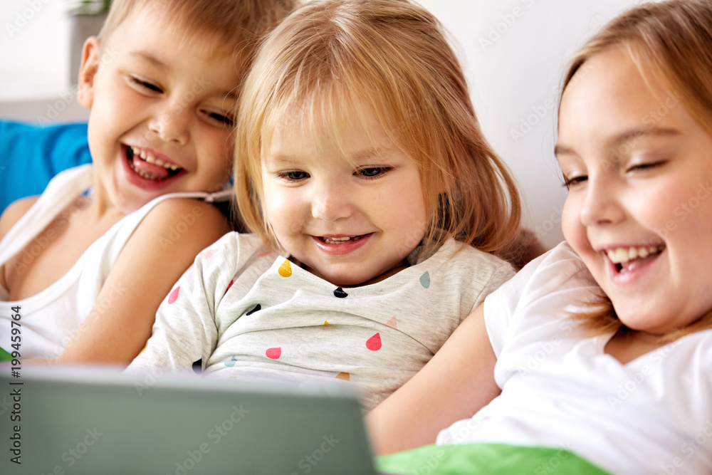 childhood, technology and family concept - happy little kids with tablet pc computer in bed at home childhood, technology and family concept - happy little kids with tablet pc computer in bed at home