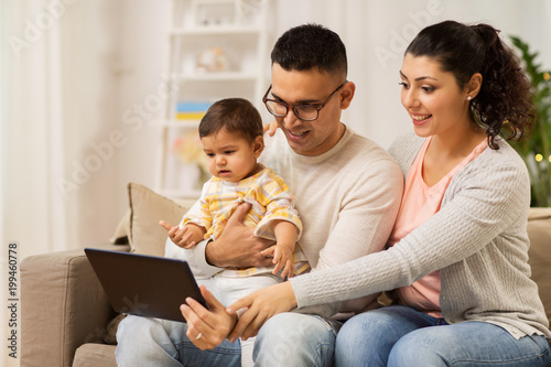 family, technology, parenthood and people concept - happy mother and father showing tablet pc computer to baby daughter at home