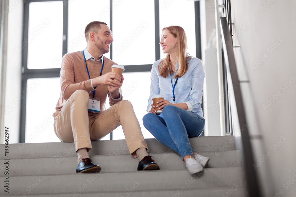 business, people and corporate concept - happy smiling man and woman with conference badges drinking coffee at office stairs
