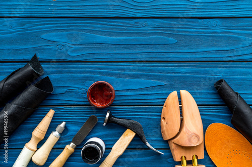 Instruments and materials for make shoes. Shoemaker's work desk. Hummer, awl, knife, sciccors, wooden shoe, insole, paint and leather. Blue wooden background top view copy space photo