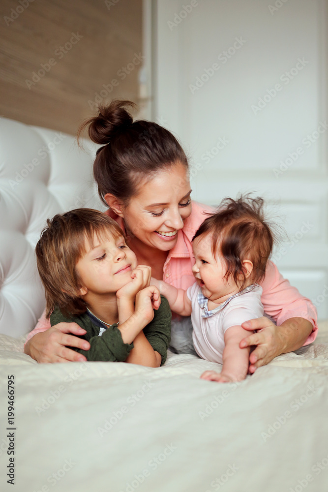 beautiful mother hugging her children at home, a small daughter and a handsome son with mom smiling and playing together