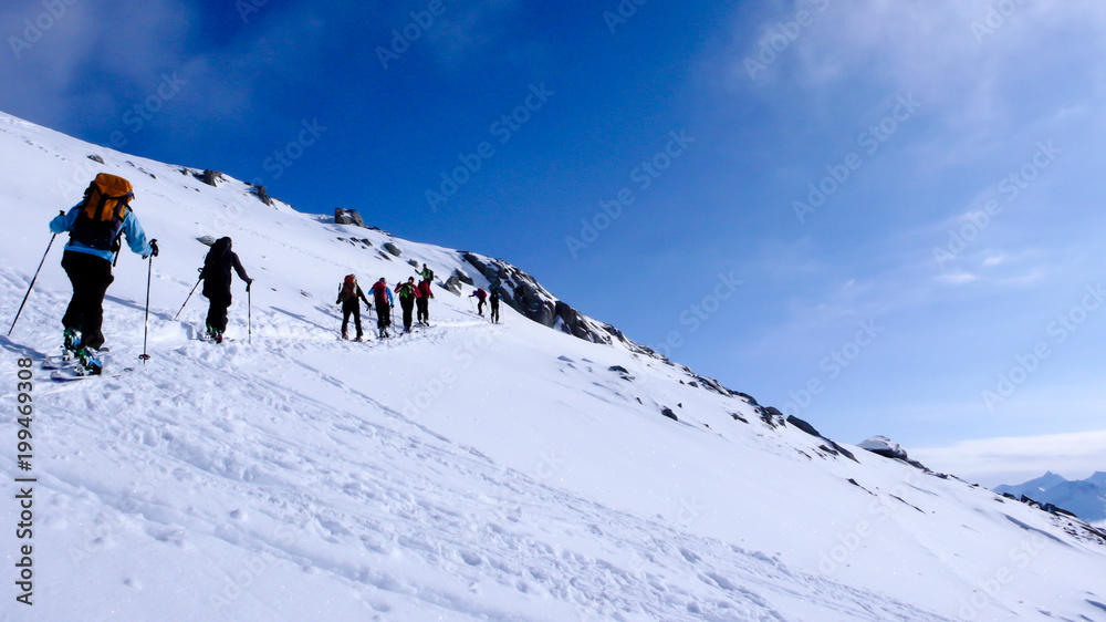 a group of backcountry skiers head towards the summit on their backcountry ski tour in the mountains of the Swiss Alps