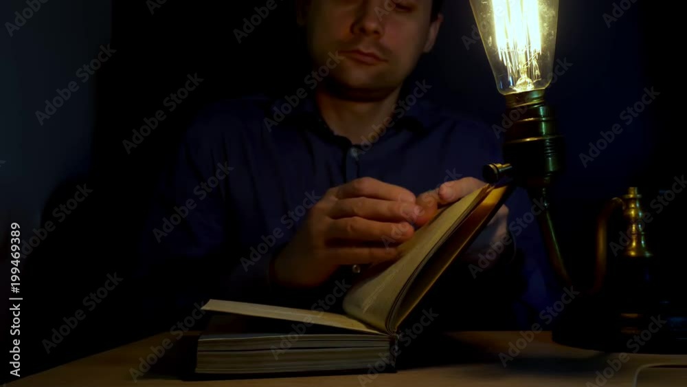 Man in a dark open old book near retro looking lamp.