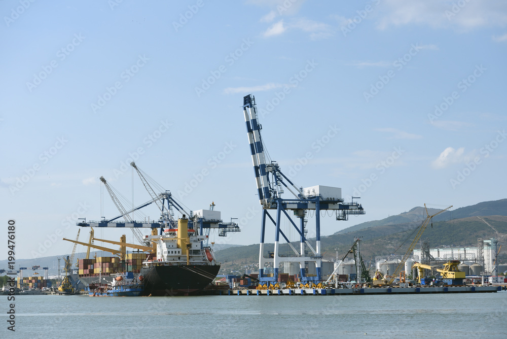 Special cranes for loading ships in the port. Loading cranes and cargo ship with containers against the background of mountains and blue sky
