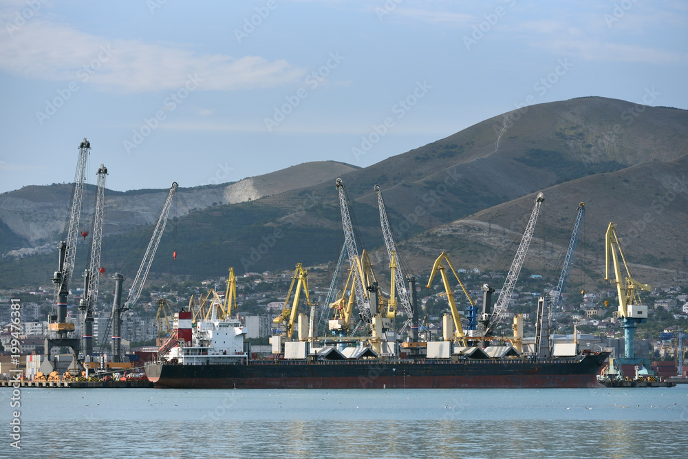 Loading cranes at the seaport unload or load a cargo ship. Cargo ship for bulk cargo in a seaport against the background of mountains