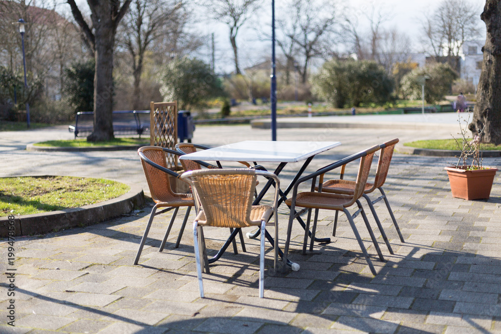 geflochtene Stapel Stühle oder Gartenstühle an einem Tisch im Freien bei sonnigem Wetter