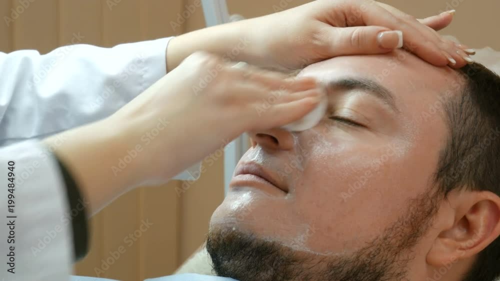 Female cosmetologist wipes face after a mask from male client Female cosmetologist wipes face after a mask from male client