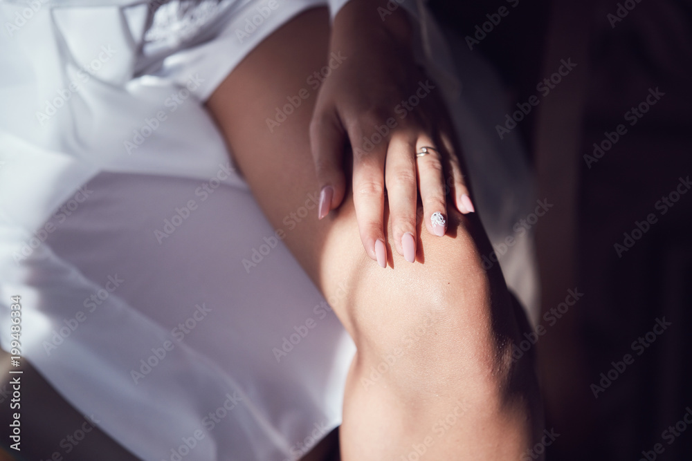 hand of a girl with a beautiful beige manicure sexually lies on her leg