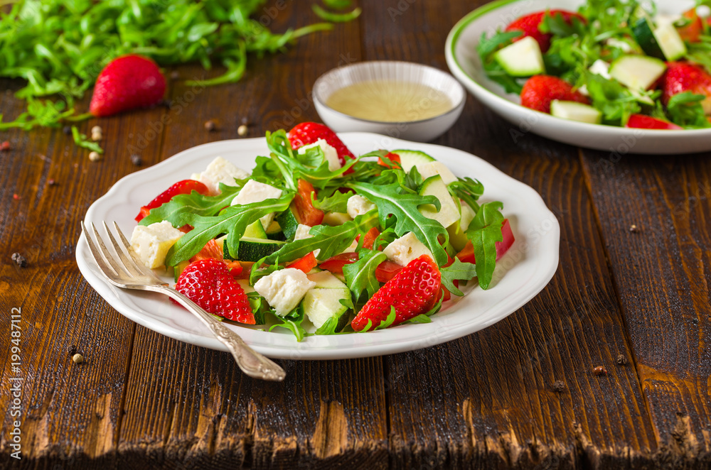 Fresh vegetable strawberry salad on white plate on natural rustic desk.