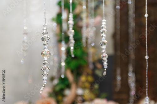 Crystal ornament hanging as a part of wedding decoration on a background of flowers and greens