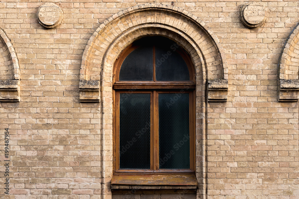 Vintage arched window in the wall of yellow brick. Black glass in a maroon dark red wooden frame. The concept of antique vintage architecture in building elements.