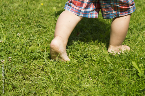 bare foots of the running toddler in the green summer grass