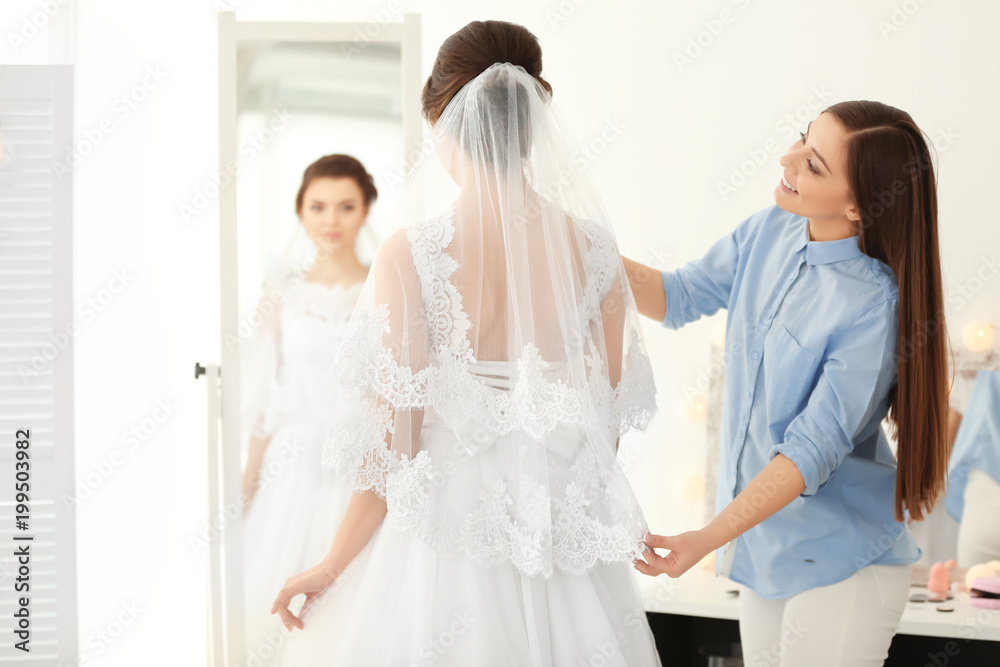Fashion stylist preparing bride before her wedding in room