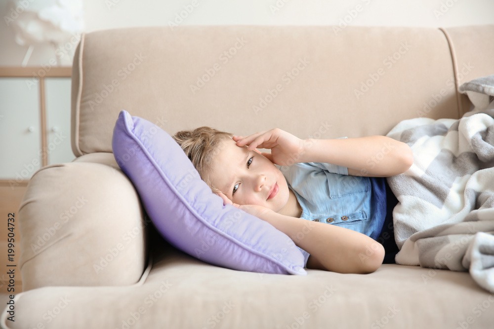 Little boy suffering from headache while lying on couch at home