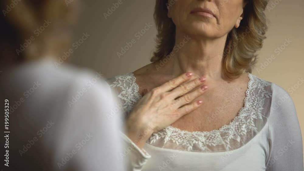 Mature female touching her wrinkled neck in front of mirror, aging process