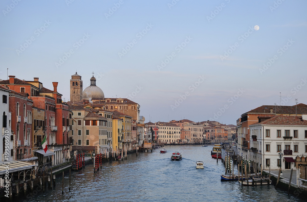 Grand Canal of Venice at dusk with full moon glowing overhead with clear blue sky.