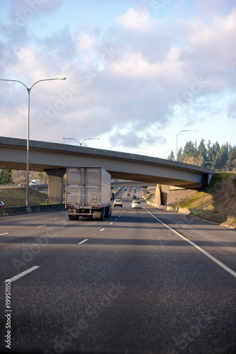 Big rig semi truck with dry van semi trailer going under the bridge across divided highway
