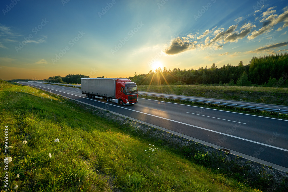 Red truck driving on the highway in the countryside in the rays of the sunset