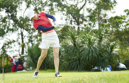 Asian woman playing golf swinging golf club for teeing off in course