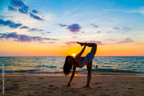 Young healthy women practicing yoga at sunset on beach