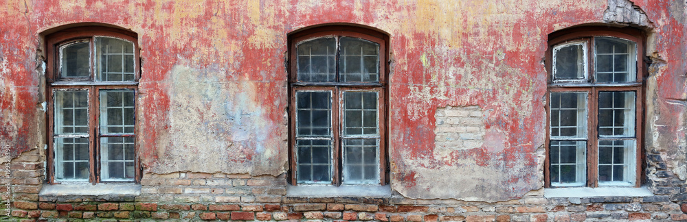 Three rotten curved windows in the red wall of a ruined old brick house.