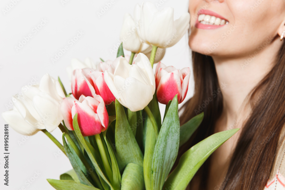 Close up cropped portrait of bright bouquet of white and pink spring tulips in hand of young smiling brunette woman in studio on white background. Concept of celebration, holiday, good mood