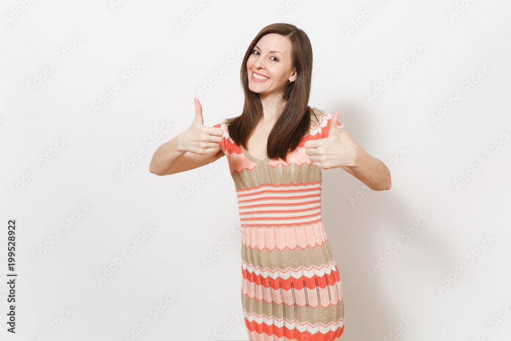 Beautiful young brunette girl in light beige and pink patterned dress rejoices, smiling and shows gestures thumbs up in studio on white background. Concept of good mood. Copy space for advertisement. Beautiful young brunette girl in light beige and pink patterned dress rejoices, smiling and shows gestures thumbs up in studio on white background. Concept of good mood. Copy space for advertisement.