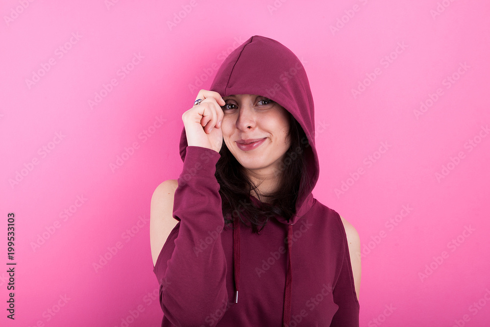 Woman with beautiful smile wears a hood on pink background in studio Woman with beautiful smile wears a hood on pink background in studio