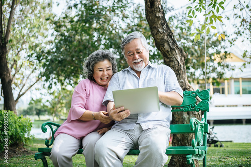 Cheerful senior woman and man using digital tablet on bench at the park