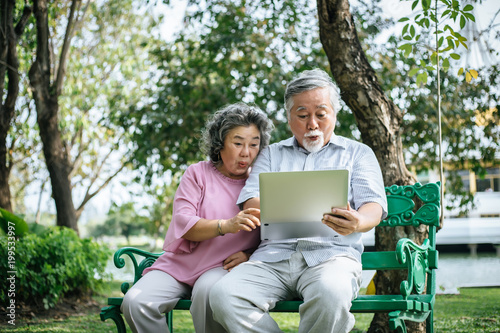 Cheerful senior woman and man using digital tablet on bench at the park