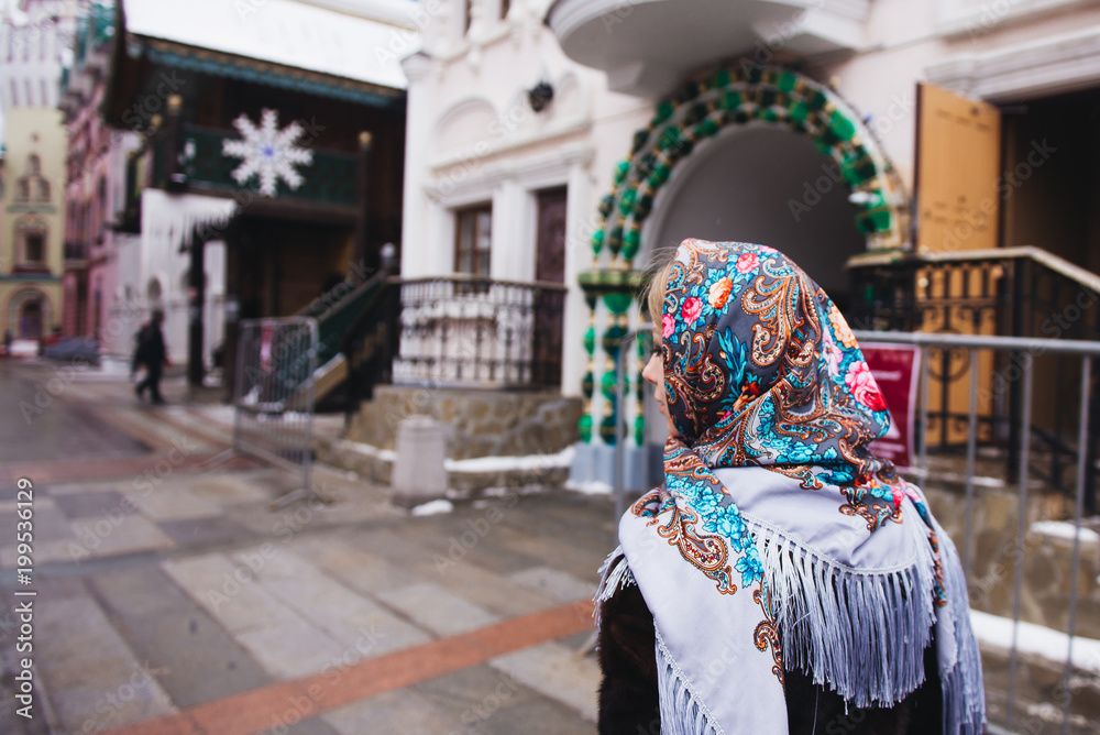A young beautiful girl in a mink coat and a Russian folk scarf walks around the Izmailovo Kremlin. Moscow, Russia.