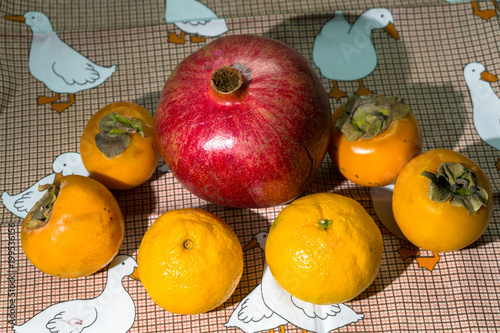 Kitchen still-life. Wholesome ripe fruits of pomegranate, mandarine and persimmon on a cute tablecloth.