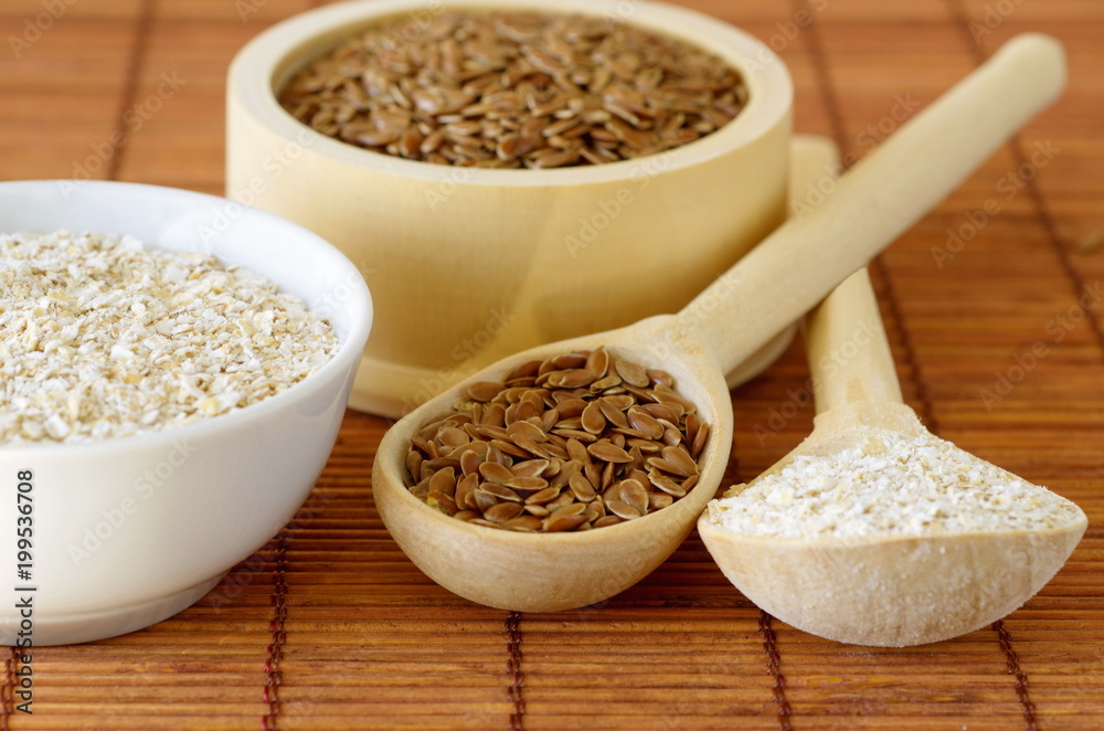 Flax seeds and oat bran in bowls and wooden spoons on bamboo napkin Flax seeds and oat bran in bowls and wooden spoons on bamboo napkin