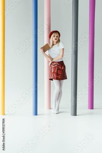 Attractive young woman holding book and posing by colorful pillars